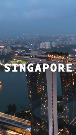 Vertical-Video-Drone-Shot-Of-Skyline-And-Waterfront-At-Dusk-Overlaid-With-Animated-Graphic-Spelling-Out-Singapore